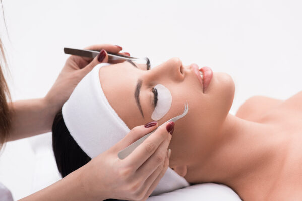 Close up of beautician arms making artificial lashes at beauty salon. Young woman is lying with relaxation and smiling. eyelash extension